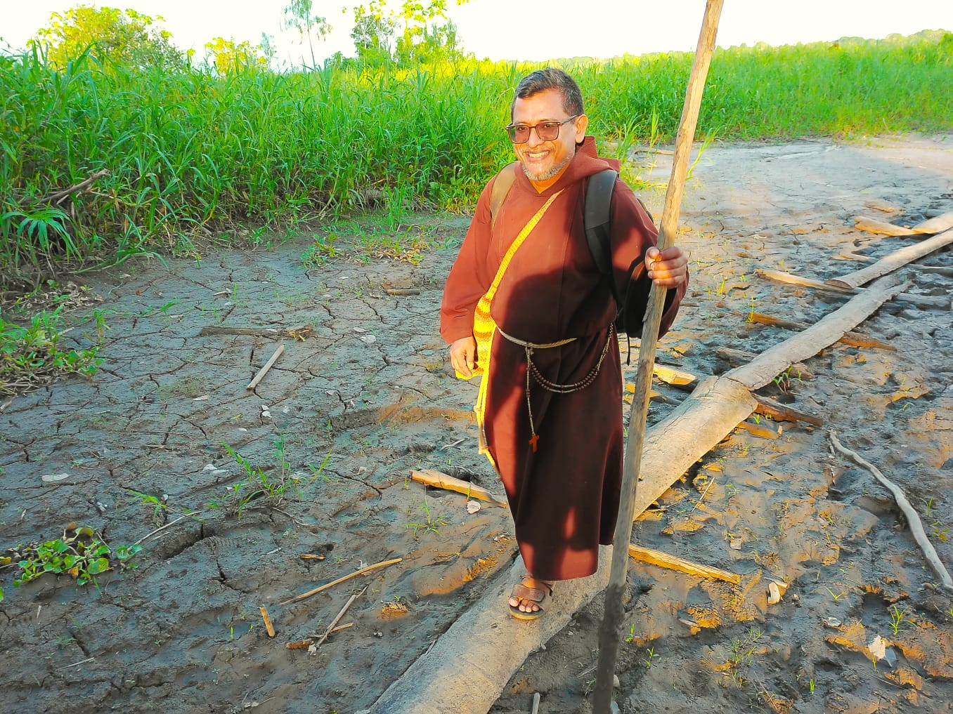 Frade caminhando pela terra rachada com cajado na mão