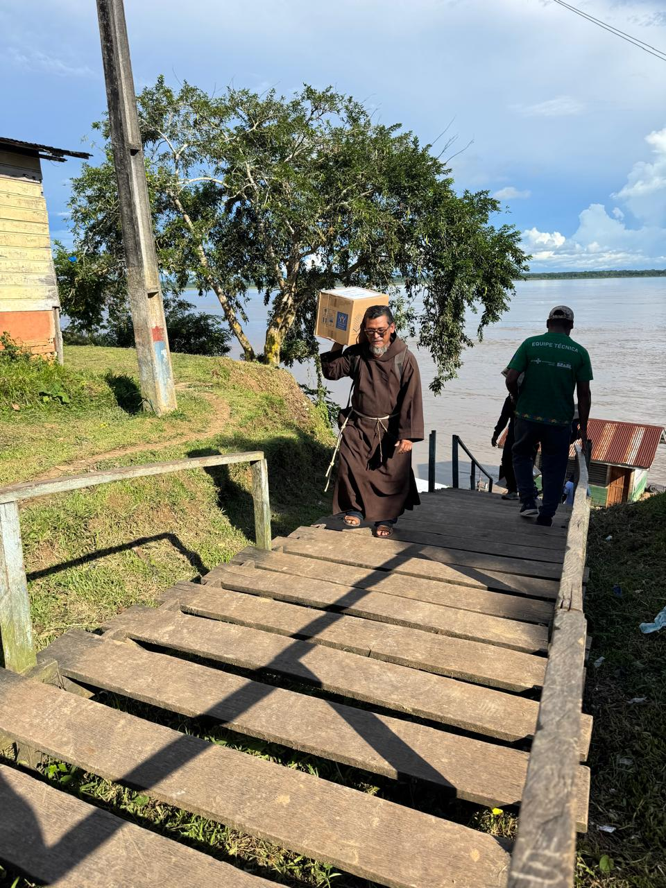 Frade subindo a escadaria com uma caixa de doações nos ombros.