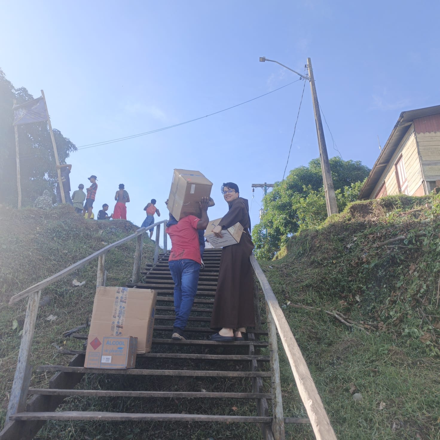 Equipe carregando caixas de doações por uma longa escadaria comunitária.
