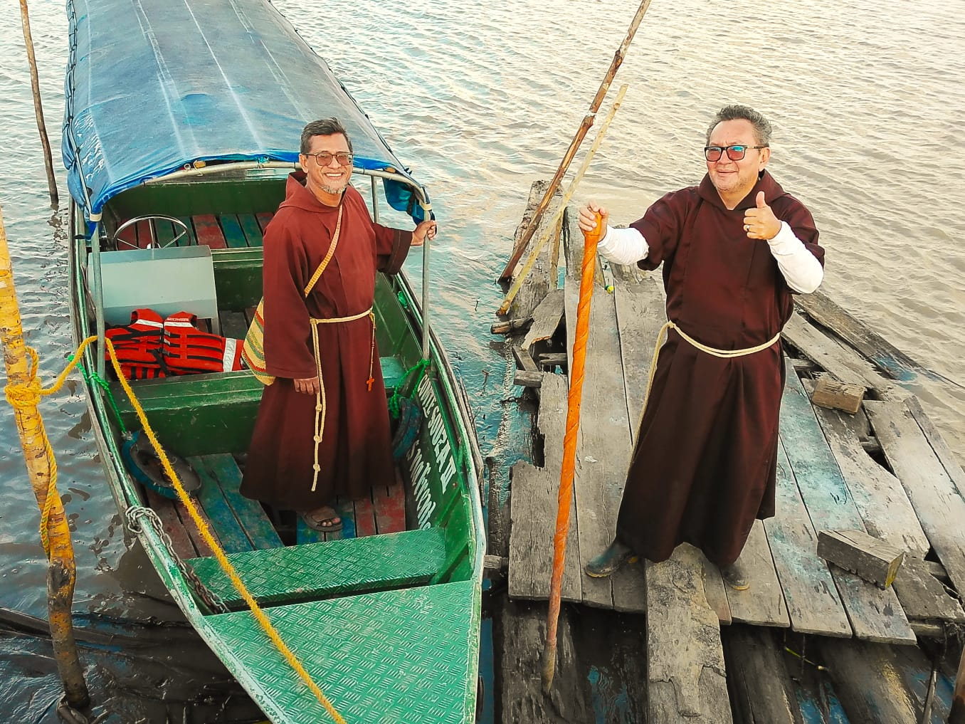 Dois frades capuchinhos junto ao barco Nossa Senhora à beira do rio