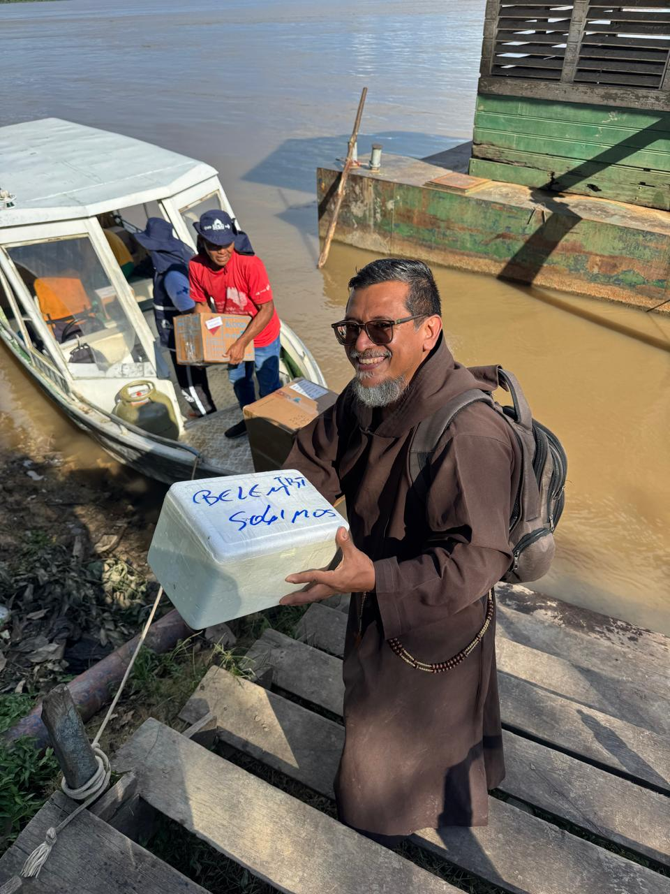 Frade sorrindo ao receber mantimentos e insumos vindos de barco.