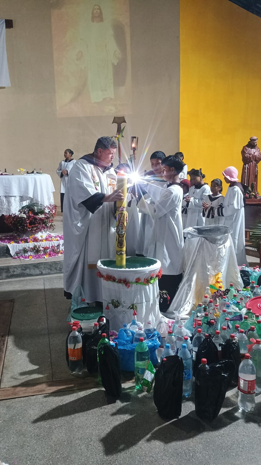 Padre acendendo o círio durante vigília com coroinhas na comunidade