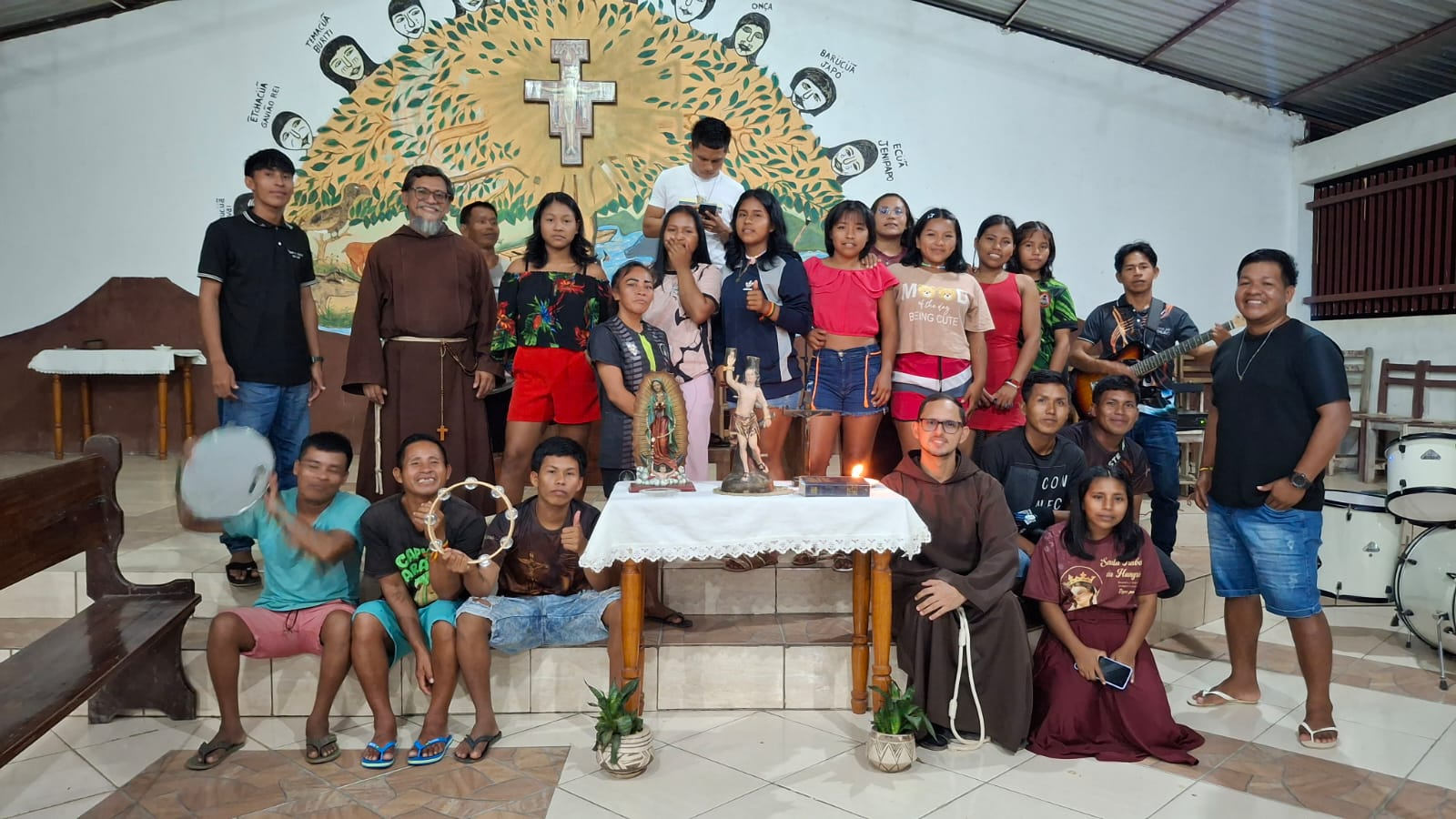 Jovens reunidos diante do altar com a cruz de São Damião e mural indígena