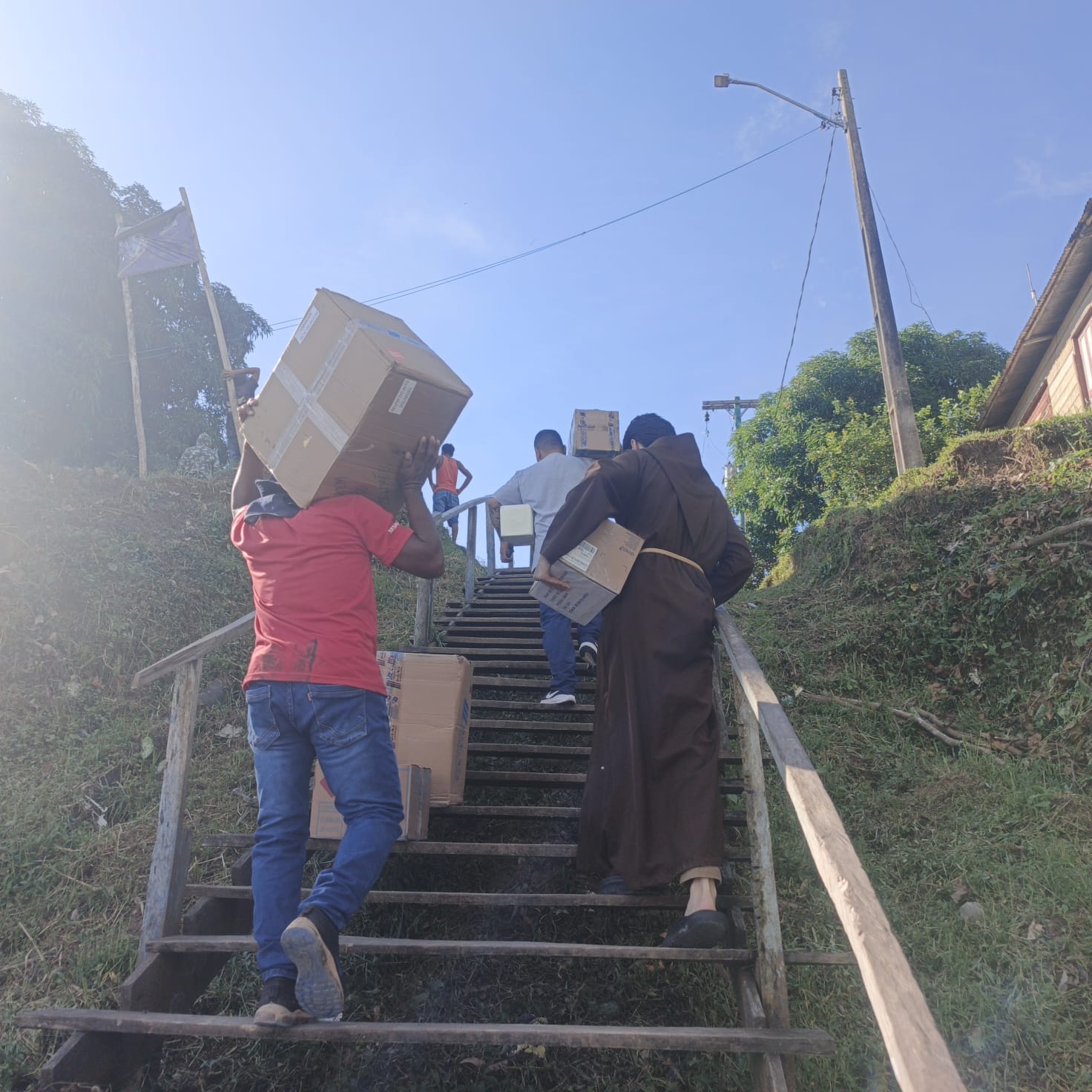 Frade e voluntários subindo escada carregando caixas de doações