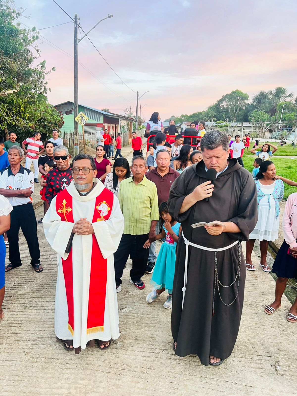 Padre e frade capuchinho conduzindo procissão pelas ruas da comunidade ao entardecer