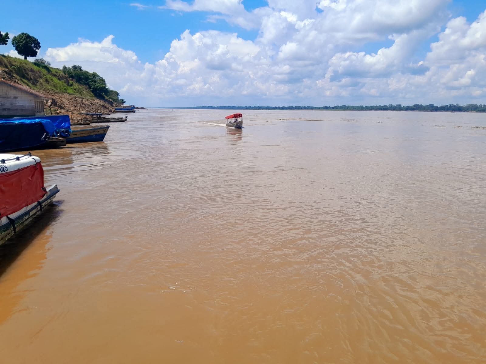 Barco navegando pelas águas barrentas do rio Solimões com o porto e a mata ao fundo